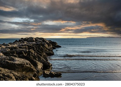 Dramatic sunset landscape photography capturing a rocky breakwater extending into the calm sea water in Italy under a cloudy sky filled with golden light and storm clouds perfect for travel backgrounds
