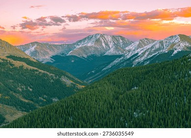 Dramatic sunset light illuminates rugged mountain peaks and dense evergreen forests at Independence Pass of the Colorado Rocky Mountains.