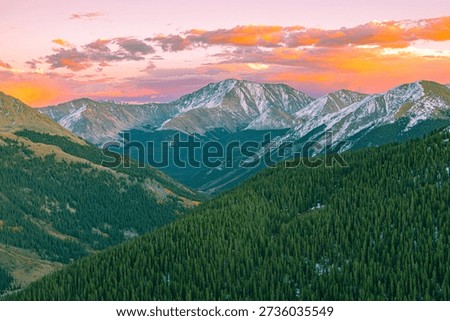 Dramatic sunset light illuminates rugged mountain peaks and dense evergreen forests at Independence Pass of the Colorado Rocky Mountains.
