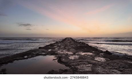 Dramatic sunset light over Atlantic jetty extending into ocean.