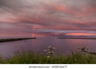 A dramatic sunset lights up the cloudy sky as a vibrant rainbow appears in Tynemouth in the North East of England
