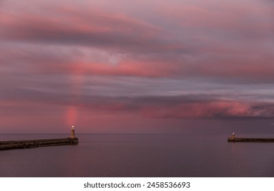 A dramatic sunset lights up the cloudy sky as a vibrant rainbow appears in Tynemouth in the North East of England