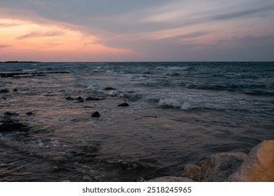 Dramatic sunset over the Adriatic Sea in Puglia. Golden-orange sky contrasts with dark clouds and deep blue waters. Rocky shoreline and silhouetted figure create a moody, contemplative coastal scene. - Powered by Shutterstock