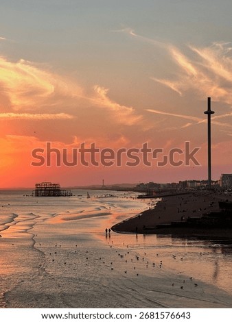 Dramatic sunset over Brighton beach, featuring the ruins of the historic West Pier, the modern British Airways i360 tower, and reflections of colorful skies on the sea