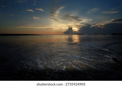 A dramatic sunset over a calm ocean with gentle waves washing ashore under a golden and blue twilight sky