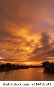 Dramatic sunset over a calm river with golden orange clouds reflecting on the water, tranquil nature landscape for travel and wellness background