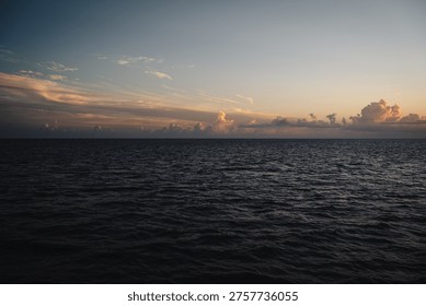 Dramatic sunset over dark deep blue ocean water and distant clouds