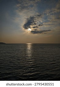 Dramatic sunset over the dark ocean with the sun hiding behind clouds and reflecting on the water surface.