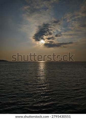 Dramatic sunset over the dark ocean with the sun hiding behind clouds and reflecting on the water surface.