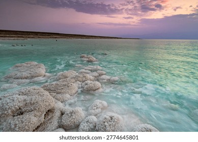 Dramatic sunset over the Dead Sea with unique salt formations along the shoreline. Calm turquoise water and mineral textures create a surreal natural landscape. Peaceful atmosphere, travel destination, wellness and nature concept.
