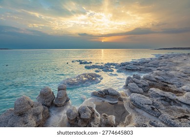Dramatic sunset over the Dead Sea with unique salt formations along the shoreline. Calm turquoise water and mineral textures create a surreal natural landscape. Peaceful atmosphere, travel destination, wellness and nature concept.