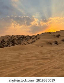 Dramatic sunset over desert sand dunes with stunning crepuscular sun rays breaking through clouds