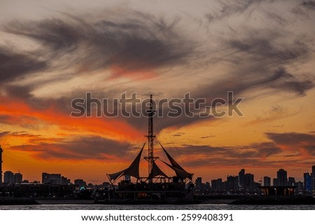 Dramatic sunset over Kuwait City's Marina Crescent, featuring the iconic Sailing Tower silhouetted against a sky filled with vibrant orange and purple hues