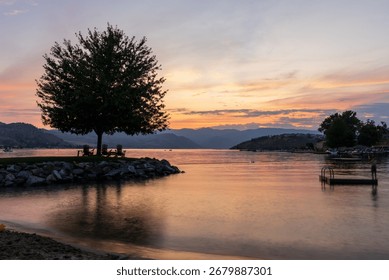 Dramatic sunset over Lake Chelan with silhouette of tree and chairs for relaxation and sky reflected in the smooth water of the lake in WA