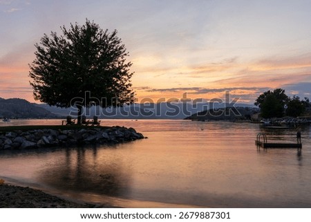Dramatic sunset over Lake Chelan with silhouette of tree and chairs for relaxation and sky reflected in the smooth water of the lake in WA