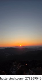 Dramatic sunset over layered mountain ranges with orange sky and distant silhouettes of hills