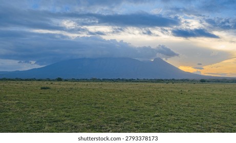 Dramatic sunset over Mount Baluran and the vast Bekol savanna grass field under cloudy sky in East Java, Indonesia. Beautiful evening landscape.