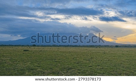 Dramatic sunset over Mount Baluran and the vast Bekol savanna grass field under cloudy sky in East Java, Indonesia. Beautiful evening landscape.
