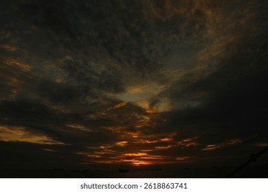 A dramatic sunset over the ocean with dark clouds filling the sky. The silhouette of a boat is seen against the vibrant orange and dark tones of the sky, creating a moody, atmospheric scene.