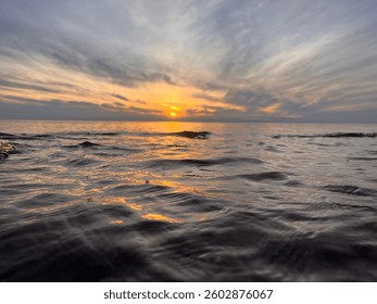 Dramatic sunset over ocean surface with glowing water reflections and moody sky. Captured from water level, ideal for nature, travel, relaxation, or inspirational themes.
