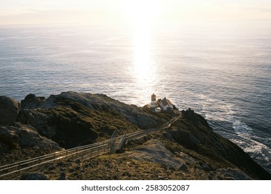 Dramatic sunset over an oceanfront lighthouse, golden light on calm waters. Cliffside beacon, rugged coastline, endless horizon, tranquil seascape, maritime navigation, scenic coastal view, solitude.