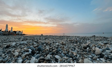 Dramatic sunset over a pebble beach with silhouettes of people and umbrellas