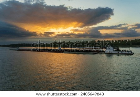 Dramatic sunset over river barge carrying coal down the Mississippi river in Baton Rouge Louisiana looking towards Port Allen