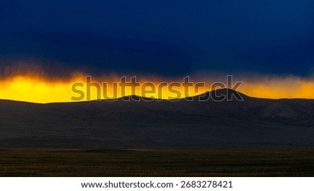 Dramatic sunset over rolling hills, glowing golden horizon beneath dark storm clouds, scenic wilderness landscape and natural beauty.