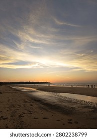 Dramatic sunset over a sandy beach with people enjoying the shoreline. Colorful evening sky with clouds reflected over the ocean, creating a peaceful tropical seascape.