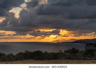 Dramatic sunset over the sea with dark clouds, sun rays and distant ships.
