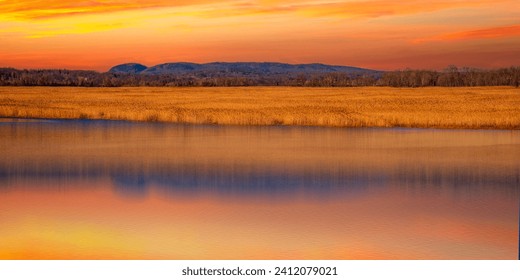 Dramatic Sunset over Sleeping Giant Mountain, Gold-colored Common Reeds Plants, and the Quinnipiac River in Hamden viewed from Tidal Marsh Trail in North Haven, Connecticut