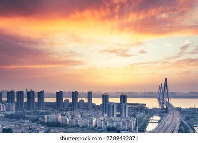 Dramatic sunset over the Yangtze River and Erqi Yangtze River Bridge in Wuhan, China, with glowing clouds above the modern city skyline.