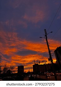 A dramatic sunset paints the evening sky with vivid shades of orange and crimson above a bustling city street. This striking urban scene captures energy, atmosphere, and the beauty of everyday life.