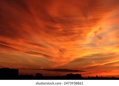 A dramatic sunset paints the sky in vibrant hues of orange and red, casting a warm glow over a distant cityscape. - Powered by Shutterstock