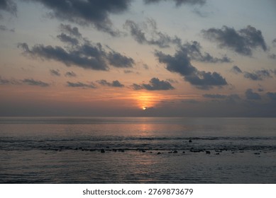 A dramatic sunset paints the sky with warm hues of orange, yellow, and pink over a calm ocean, reflecting the colors on the water's surface.