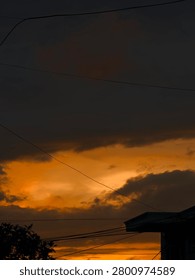 Dramatic sunset scene featuring glowing orange skies beneath dark storm clouds. Silhouettes of buildings, trees, and power lines create a striking urban landscape during the golden hour, capturing the beauty of nature and city life.