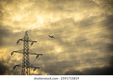 A dramatic sunset scene featuring a silhouetted electricity pylon and power lines against a golden, cloudy sky, with an airplane flying in the distance.

