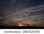 A dramatic sunset scene with a mountain silhouette beneath streaked clouds and fading light, capturing a peaceful yet powerful evening landscape.