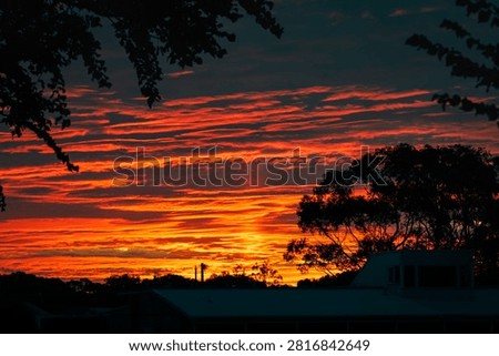 Dramatic sunset sky ablaze with layers of fiery orange, crimson and deep red clouds streching across the horizon, with silhouetted roof line in the foreground, Terang, Victoria, Australia