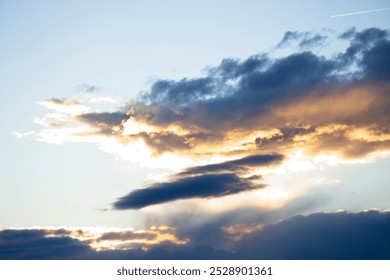 A dramatic sunset sky with clouds illuminated by golden rays, creating a striking contrast between light and shadow.                               