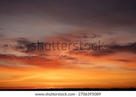 Dramatic sunset sky creating a vibrant natural background with warm orange, red, and yellow colors above a dark silhouette horizon, presenting a peaceful and atmospheric scene