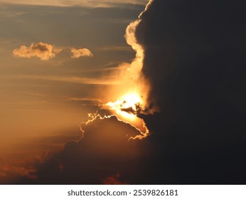 Dramatic sunset sky with dark clouds partially obscuring the sun, casting golden and orange hues across the horizon.