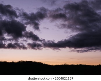 dramatic sunset sky dark clouds over silhouetted hillside at twilight