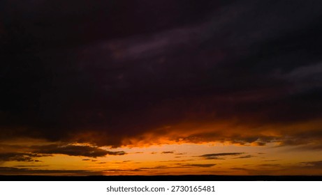 Dramatic sunset sky with dark clouds and glowing horizon. Dark moody sunset sky without land, cinematic natural background with copy space for design.