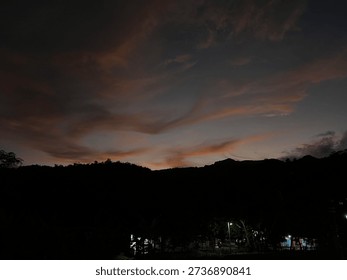 Dramatic sunset sky with dark clouds over hill silhouettes, creating emotional and peaceful evening atmosphere in nature.
