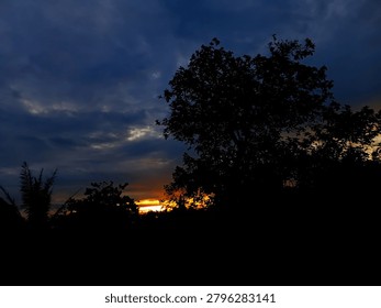 Dramatic sunset sky with dark clouds and silhouetted trees in the foreground