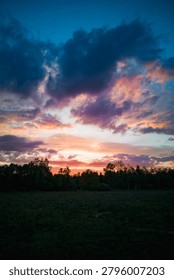 Dramatic Sunset Sky with Dark Storm Clouds and Orange Horizon Glow Over Silhouetted Trees Moody Twilight Nature Landscape Before Rain Background