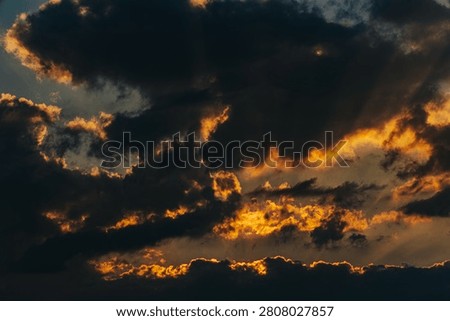 Dramatic sunset sky features dark clouds illuminated by golden sunlight, creating a vivid contrast against the deep blue evening sky