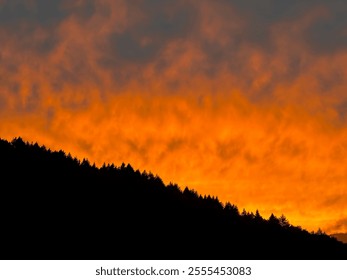 Dramatic Sunset Sky with Fiery Orange Clouds Over a Silhouetted Forested Mountain Ridge at Dusk - Powered by Shutterstock