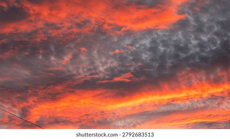 Dramatic sunset sky filled with dark grey altocumulus clouds illuminated by vibrant orange and red sunlight from beneath.
